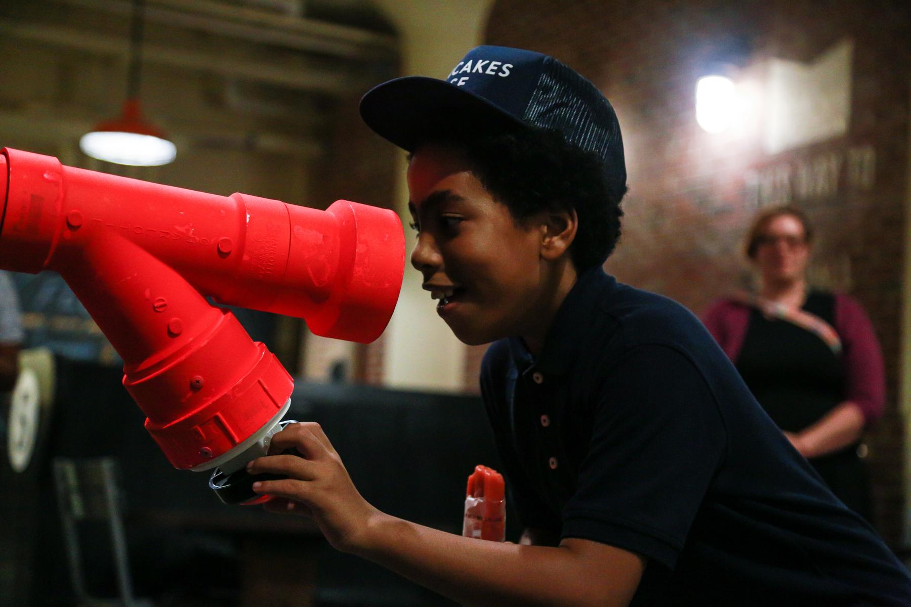 Photograph of a young boy talking into a pink tube that is part of an interactive sound sculputer at Ponce City Market, Atlanta.